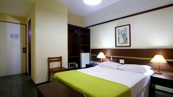 A hotel room with a bed, bedside lamps, a bench, a wardrobe, and a painting on the wall.