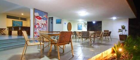 A spacious dining area with a long table and multiple chairs, a large abstract painting on the wall, and a small indoor garden with rocks and plants.