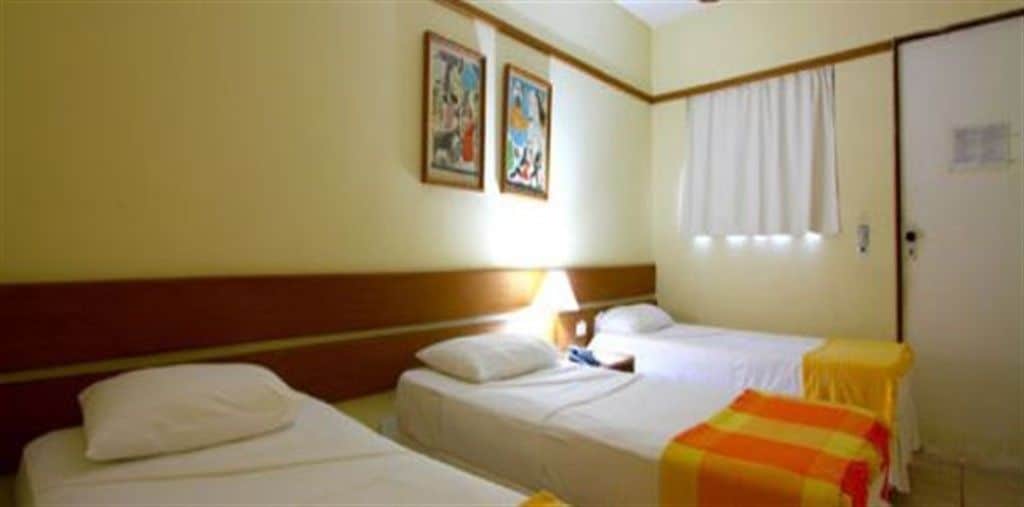 Una habitación de hotel con dos camas individuales, una mesita de noche, una lámpara y un ventanal con cortinas.