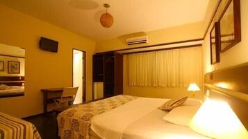 A hotel room with a bed, a bedside lamp, an air conditioning unit, a wardrobe, and a door.