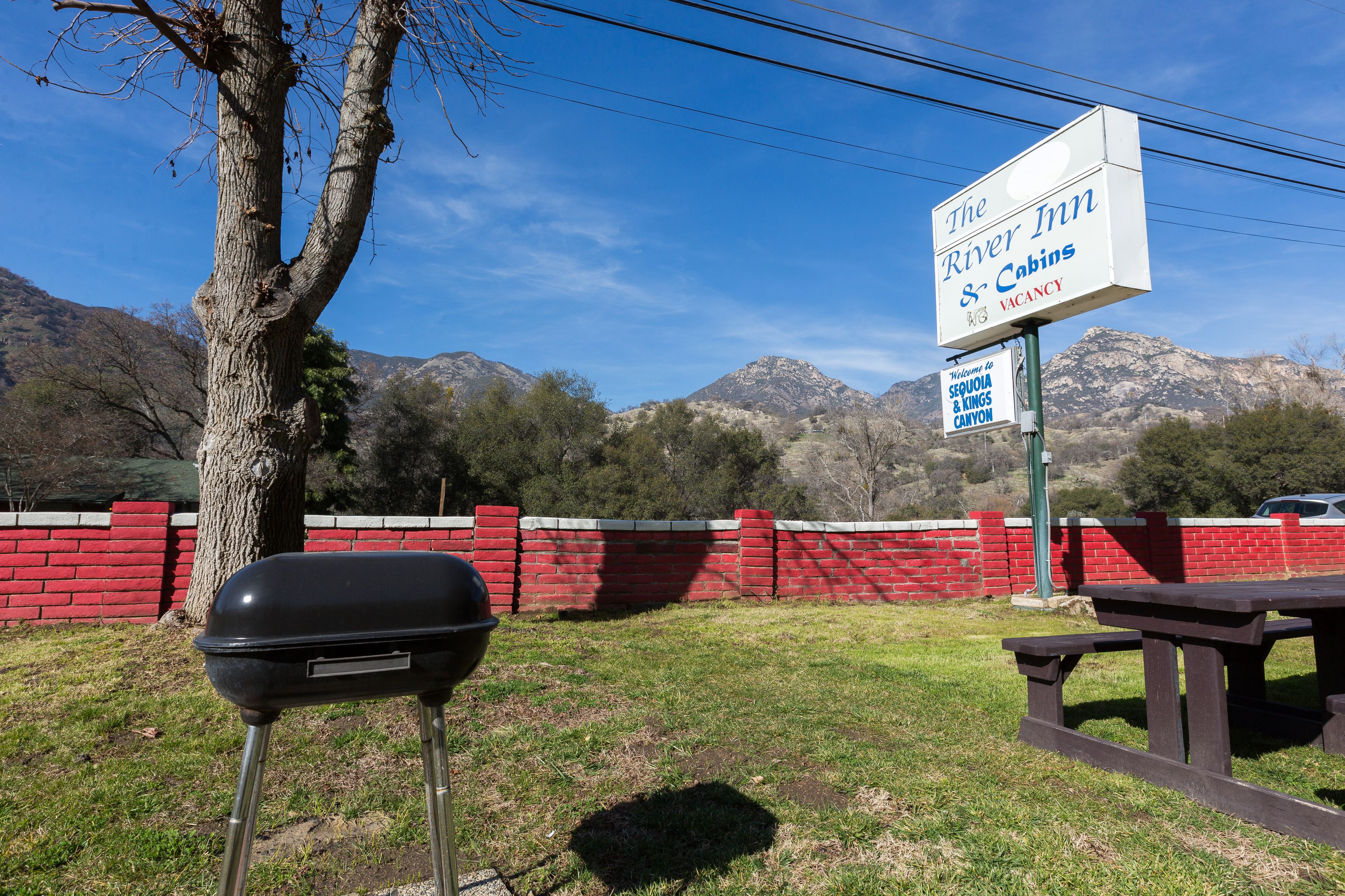 Una parrilla, una mesa de picnic y un cartel de The River Inn & Cabins, con montañas al fondo.