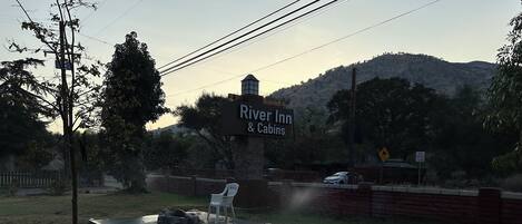 A sign for River Inn & Cabins with a view of a hilly landscape in the background.