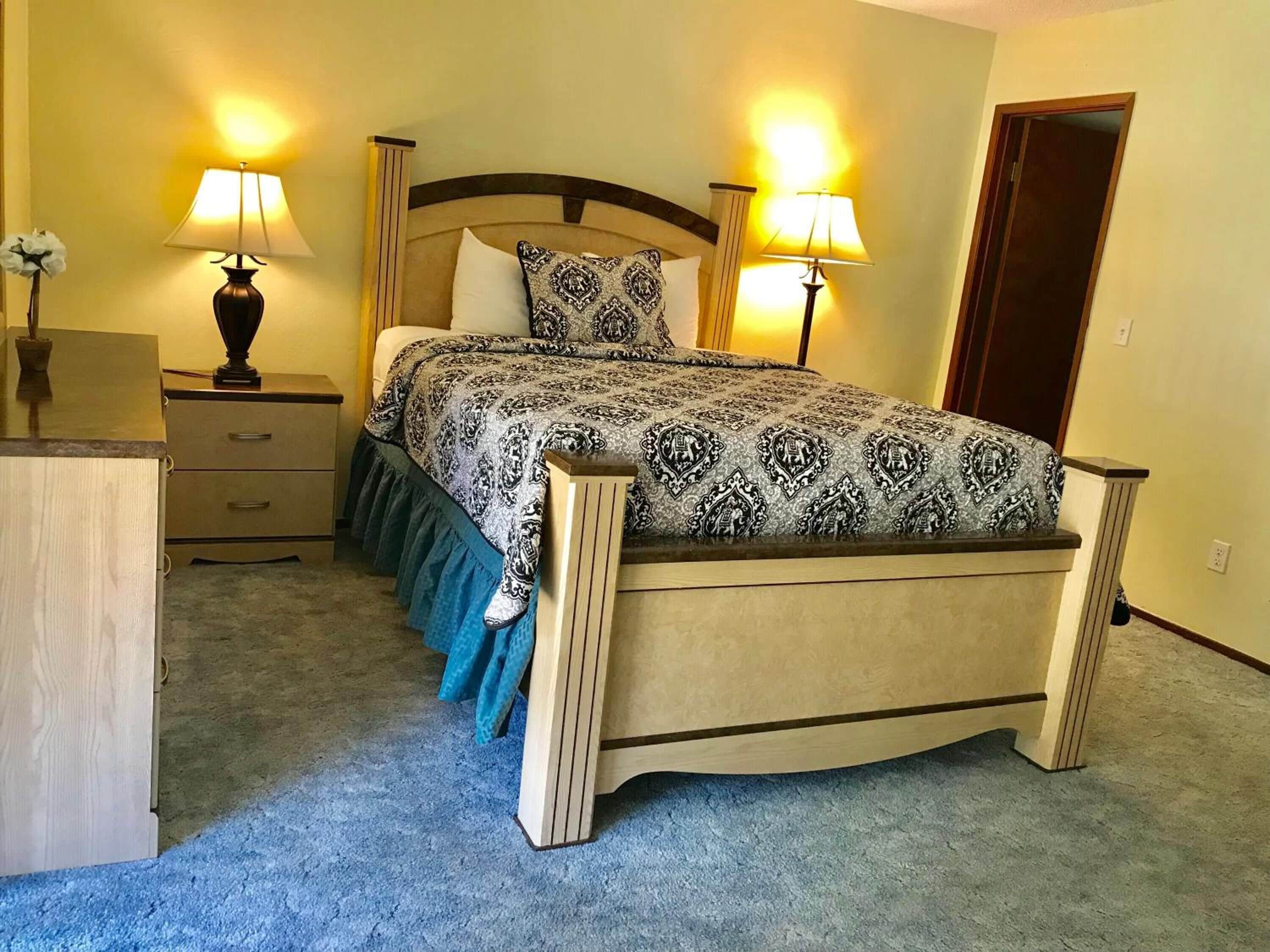 A neatly made bed with a patterned bedspread and pillows, flanked by two bedside lamps and a nightstand with a lamp.
