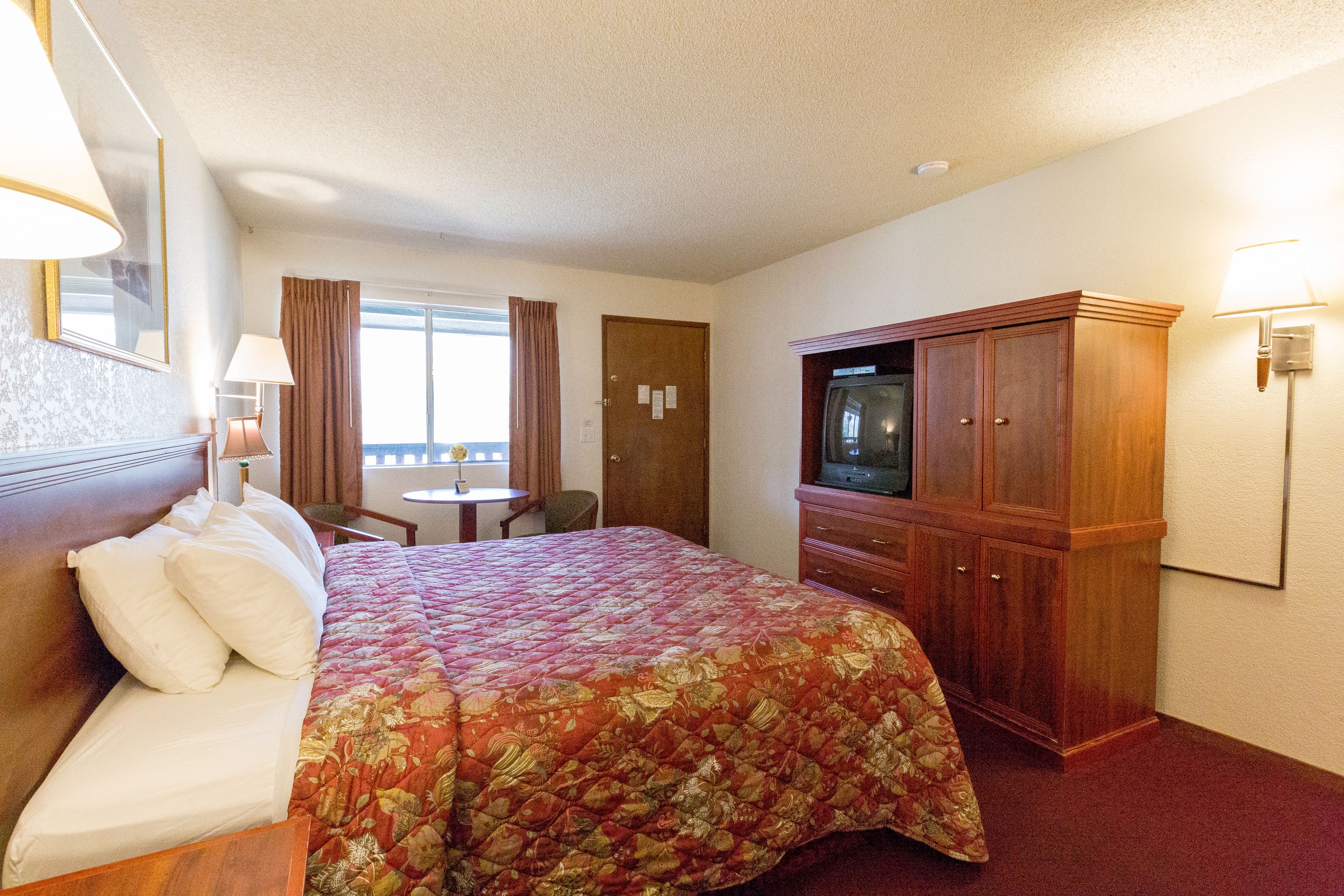 A hotel room with a large bed, a wooden cabinet, a television, and a desk with a chair.