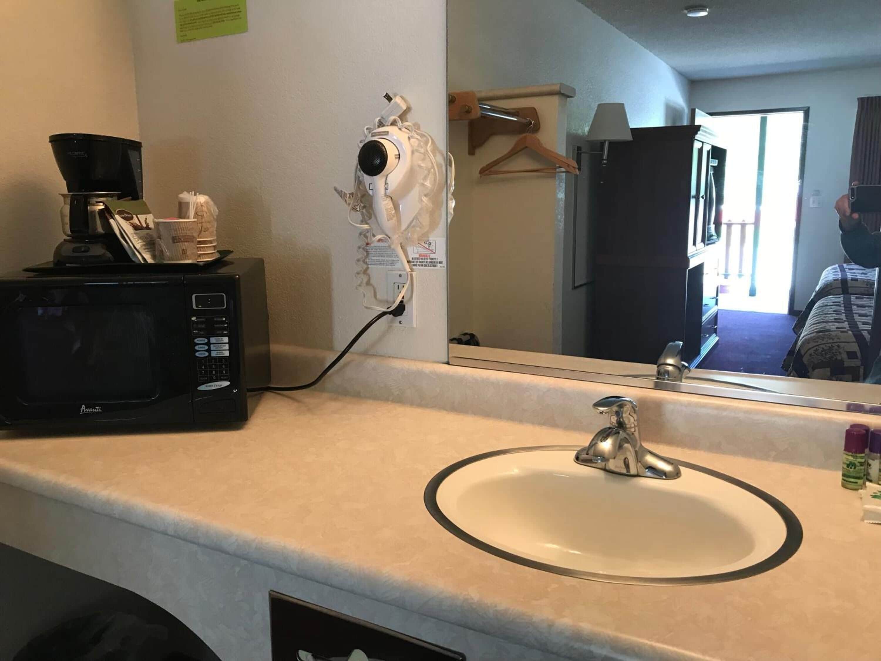 Un baño de hotel con lavamanos, espejo, secador de pelo y cafetera sobre el mostrador.