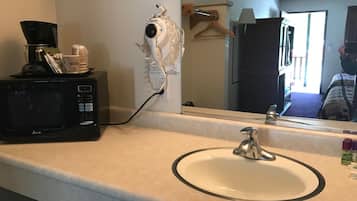Un baño de hotel con lavamanos, espejo, secador de pelo y cafetera sobre el mostrador.