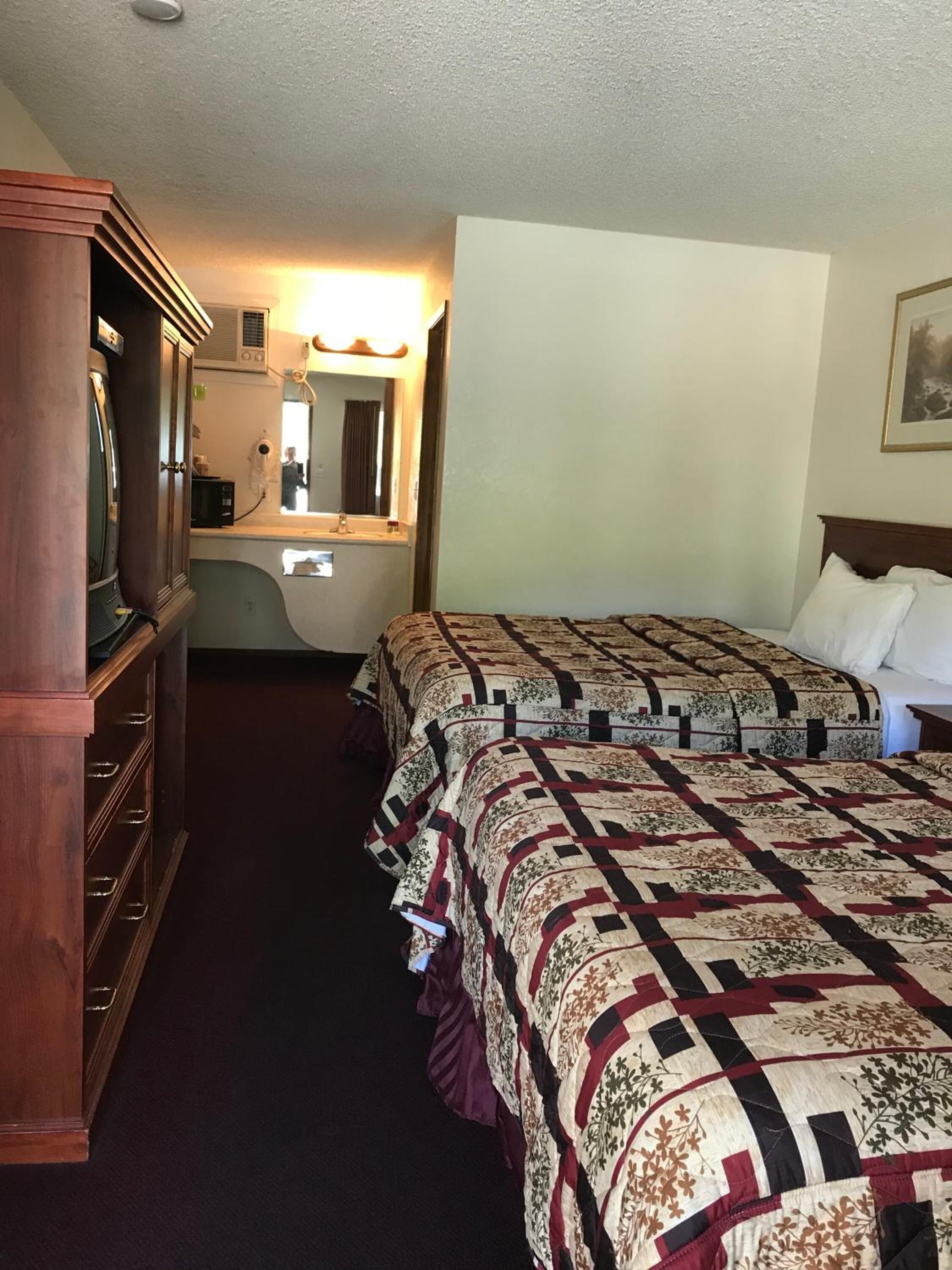 Une chambre d’hôtel avec deux lits, une commode, une coiffeuse avec un miroir et un luminaire au plafond.