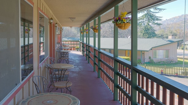 A covered outdoor area with tables and chairs, a railing, and hanging flower baskets. - The River Inn (Three Rivers)