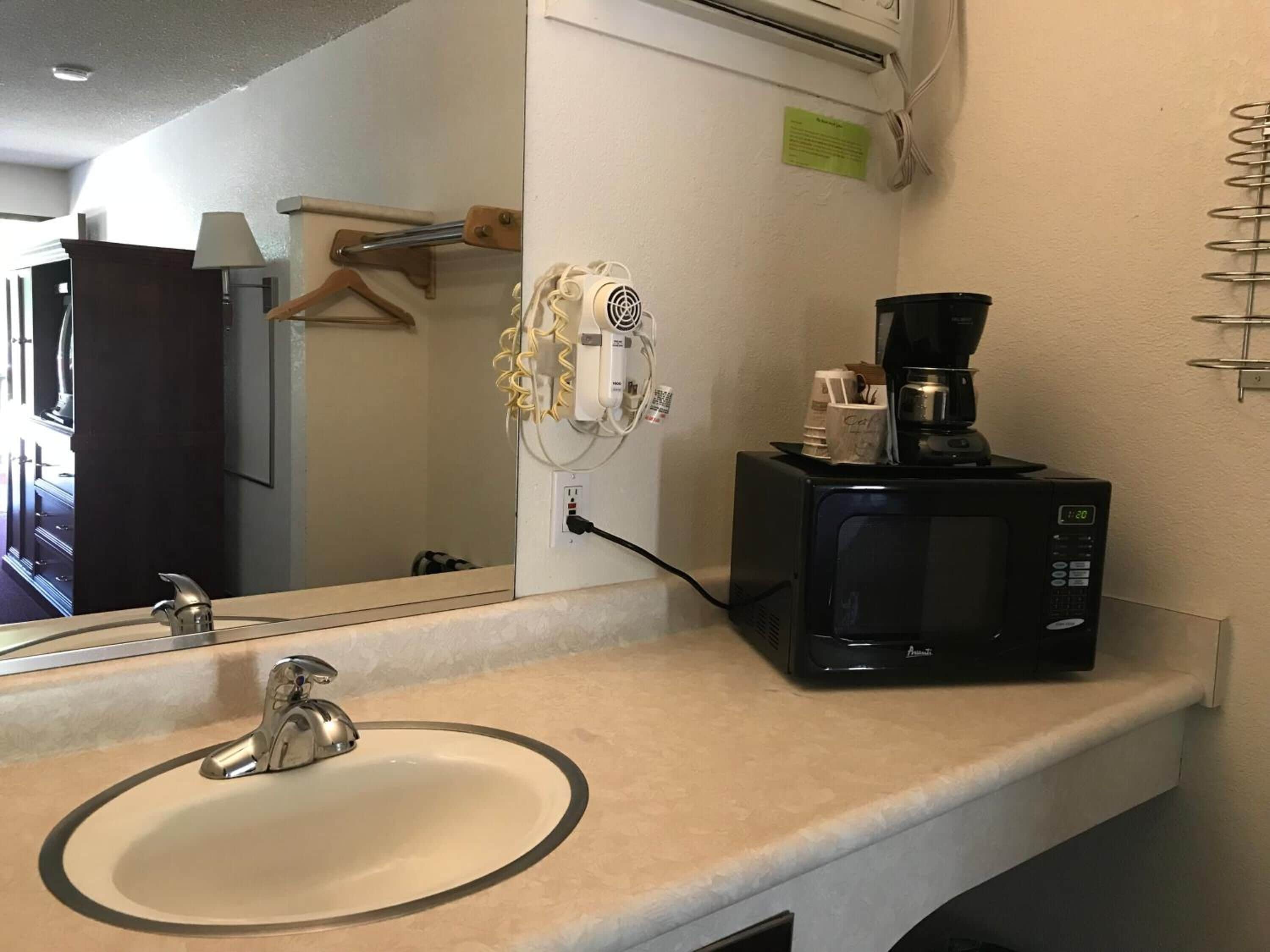 Une salle de bain équipée d’un lavabo, d’un miroir et d’une machine à café posée sur le comptoir.