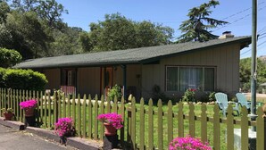 A single-story house with a porch, a fenced yard, and potted plants. - The River Inn (Three Rivers)