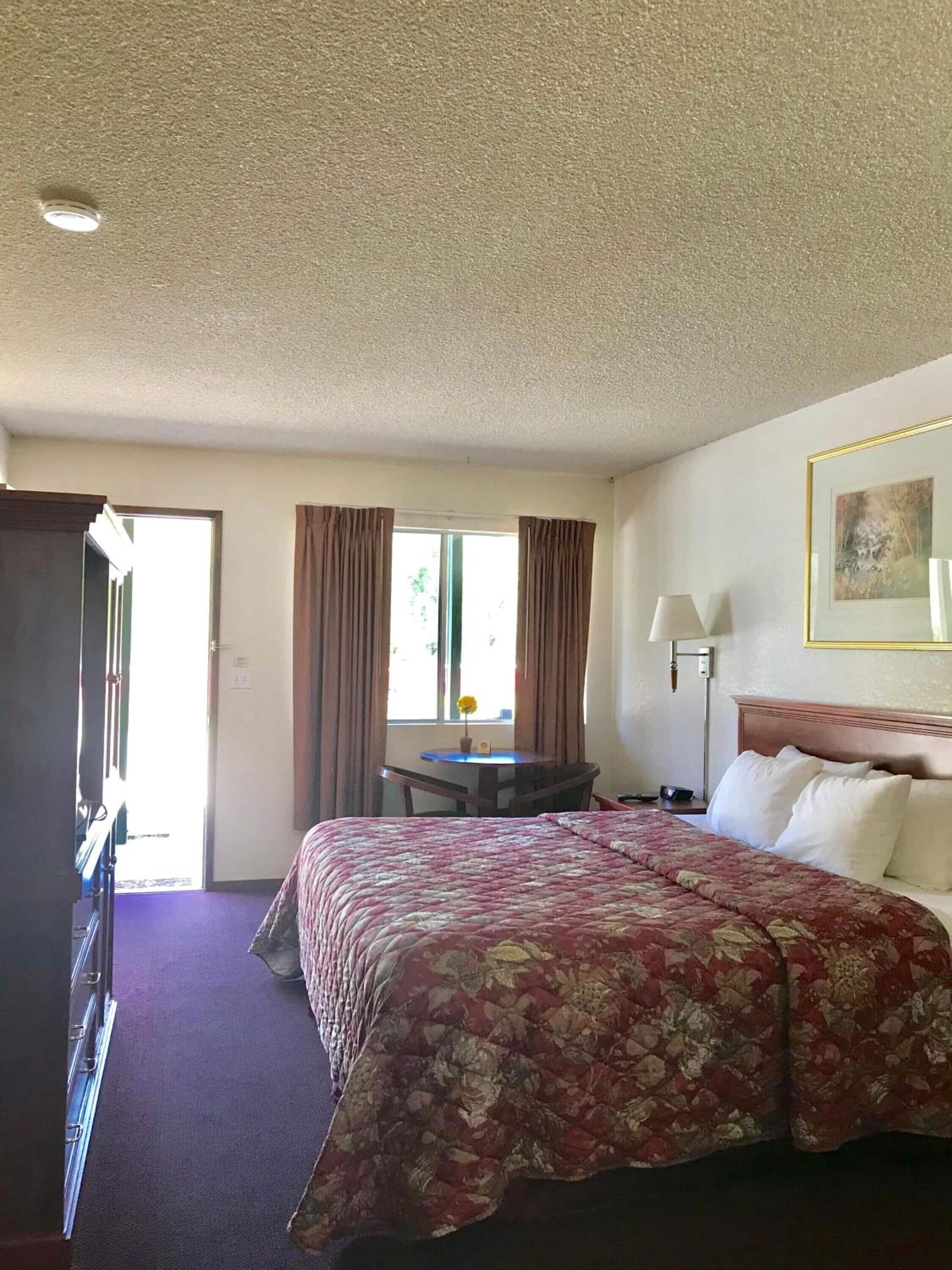 Una habitación de hotel con una cama grande, un escritorio, una silla, una lámpara y un cuadro en la pared.