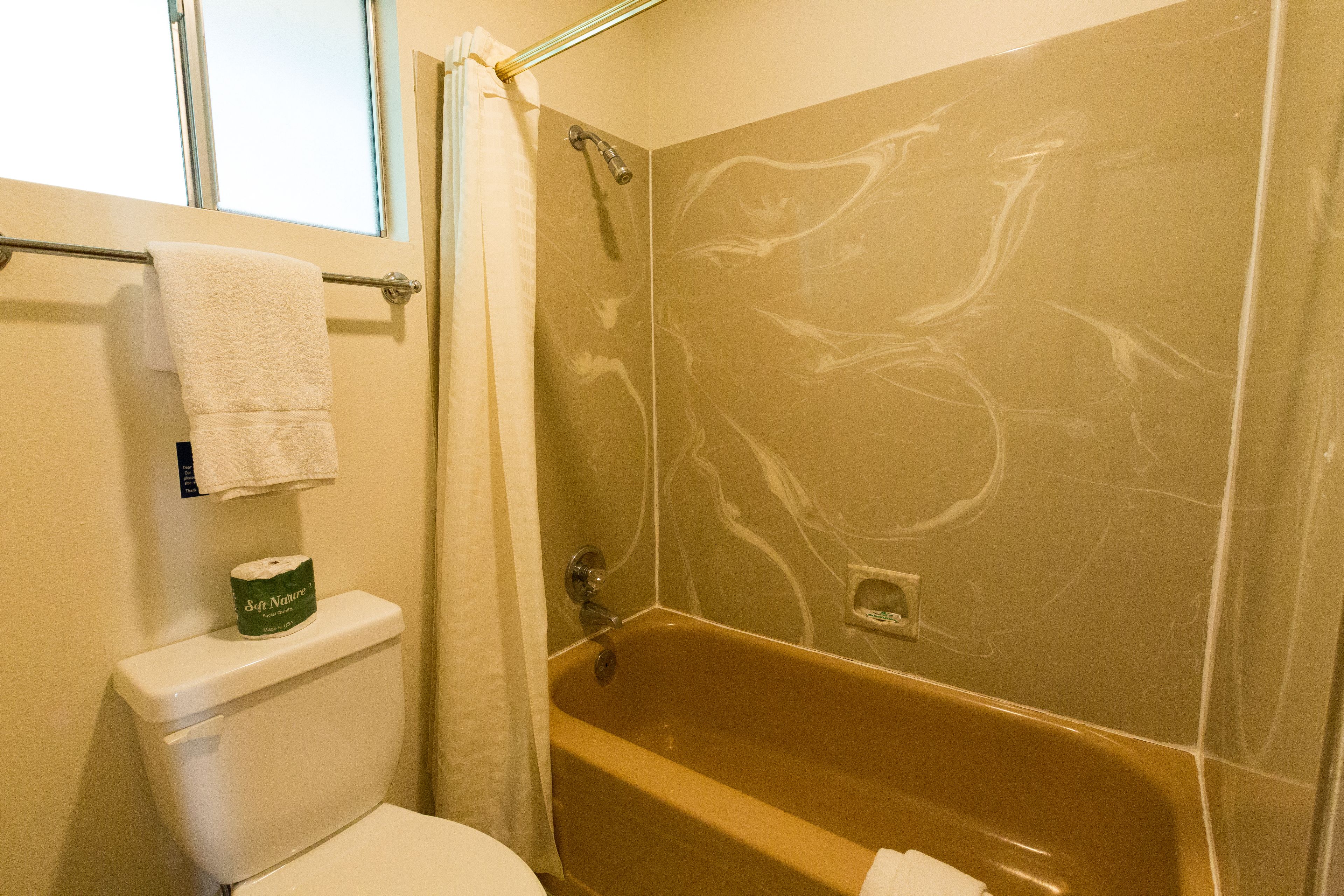 A bathroom with a bathtub, toilet, and a window.