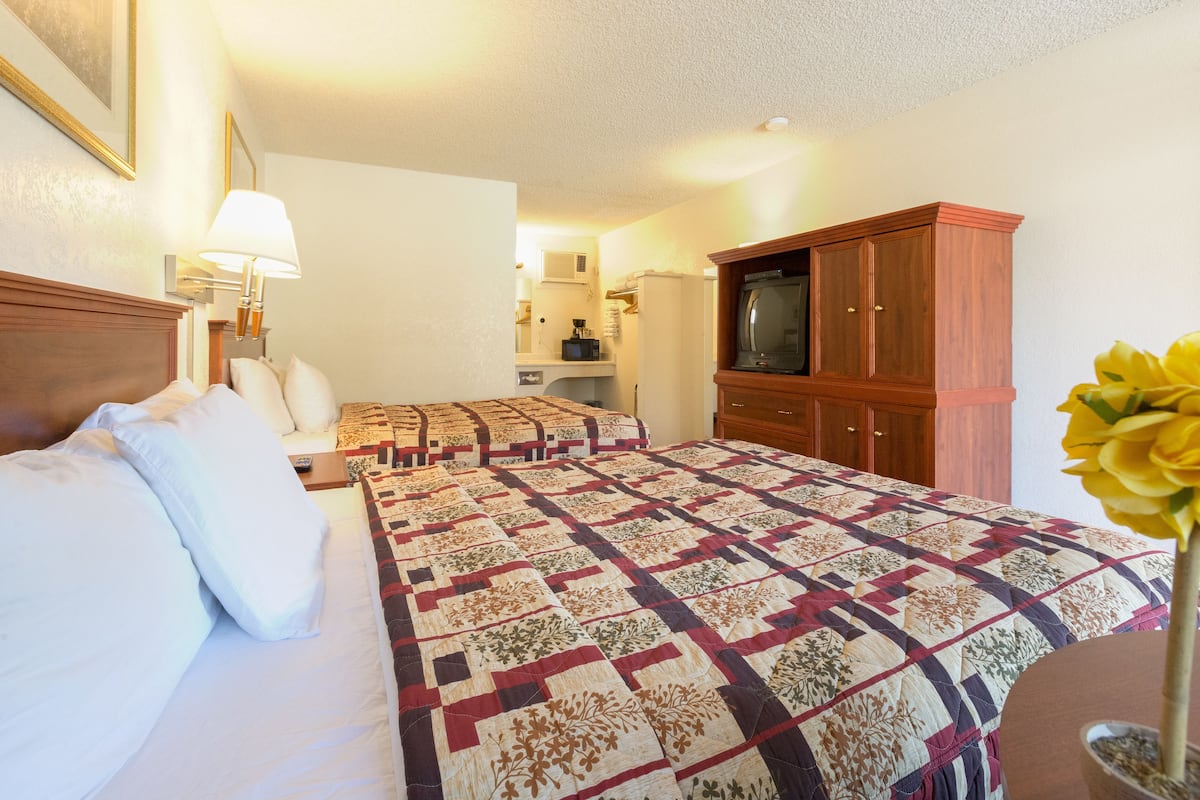A hotel room with two beds, a TV, a wooden cabinet, and a vase with flowers.