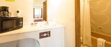 A bathroom with a white sink, a microwave, a coffee maker, and a shower with a glass door.