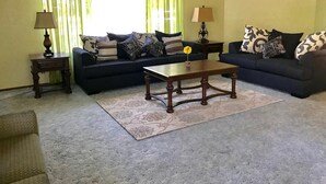 A living room with two sofas, a coffee table, a lamp, and a window with curtains. - The River Inn (Three Rivers)