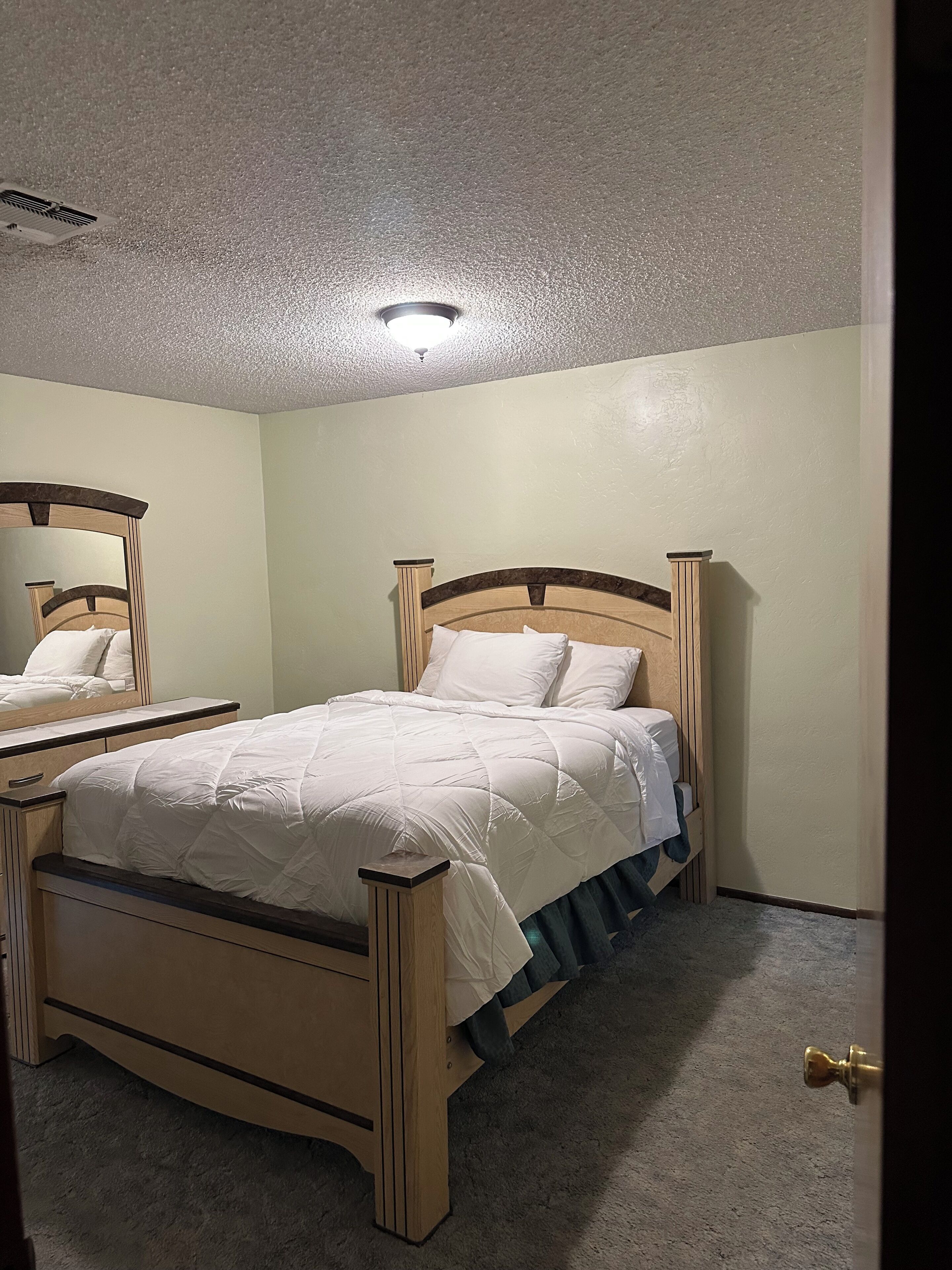 A bedroom with a wooden bed, a nightstand, a mirror, and a ceiling light.