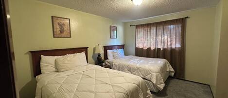 Een hotelkamer met twee bedden, een plafondlamp en een raam met gordijnen.