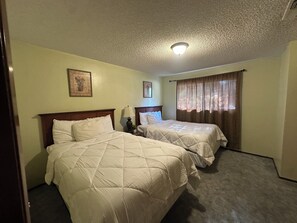 Habitación de hotel con dos camas, una lámpara en el techo y una ventana con cortinas.