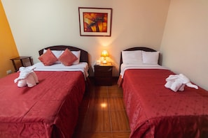 A hotel room with two beds, each with a red bedspread and white pillows. There is a nightstand with a lamp between the beds, and a framed picture on the wall above the nightstand. - Plaza Trujillo Hotel (Trujillo)