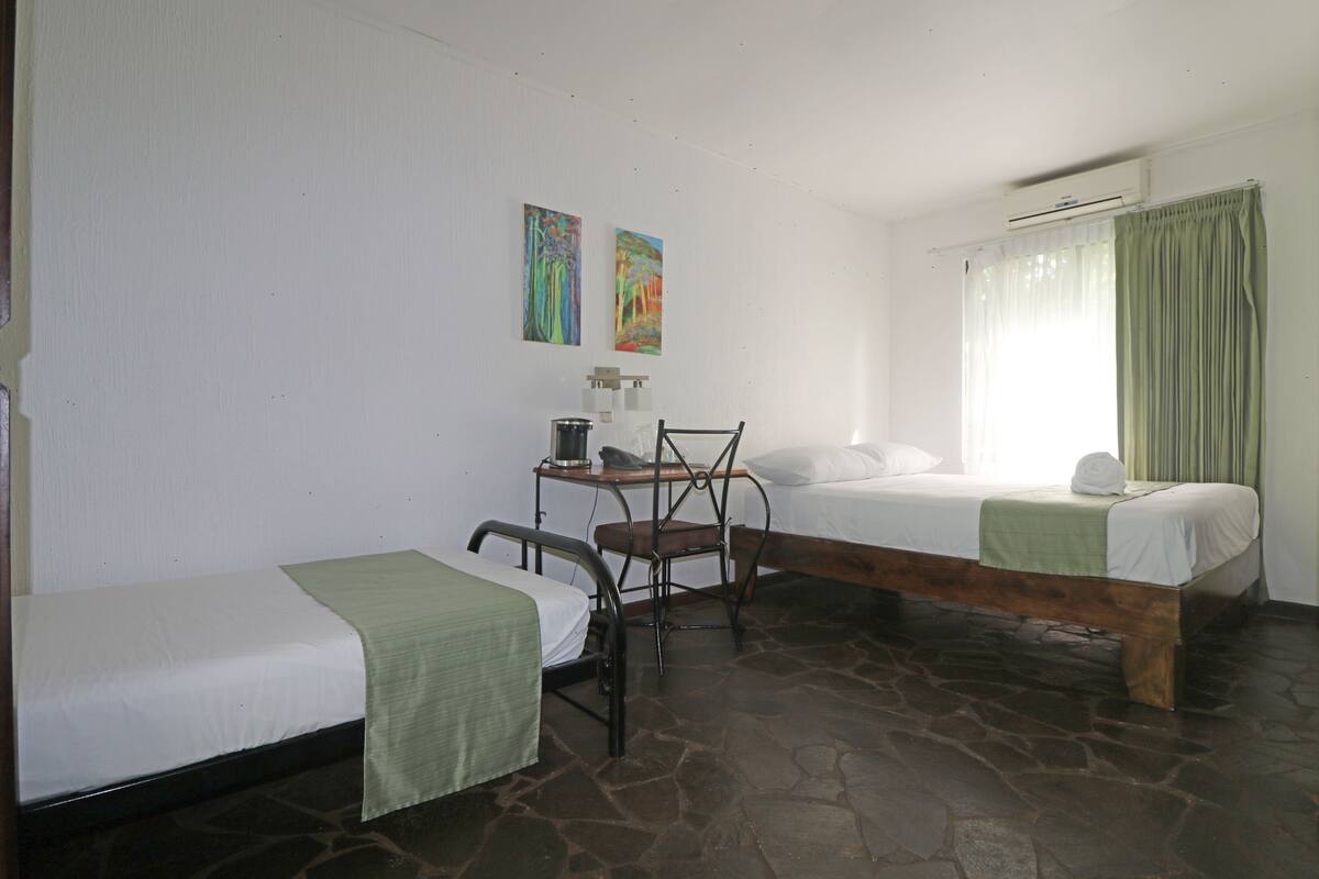 Una habitación con dos camas individuales, una mesita con una silla y dos cuadros en la pared.
