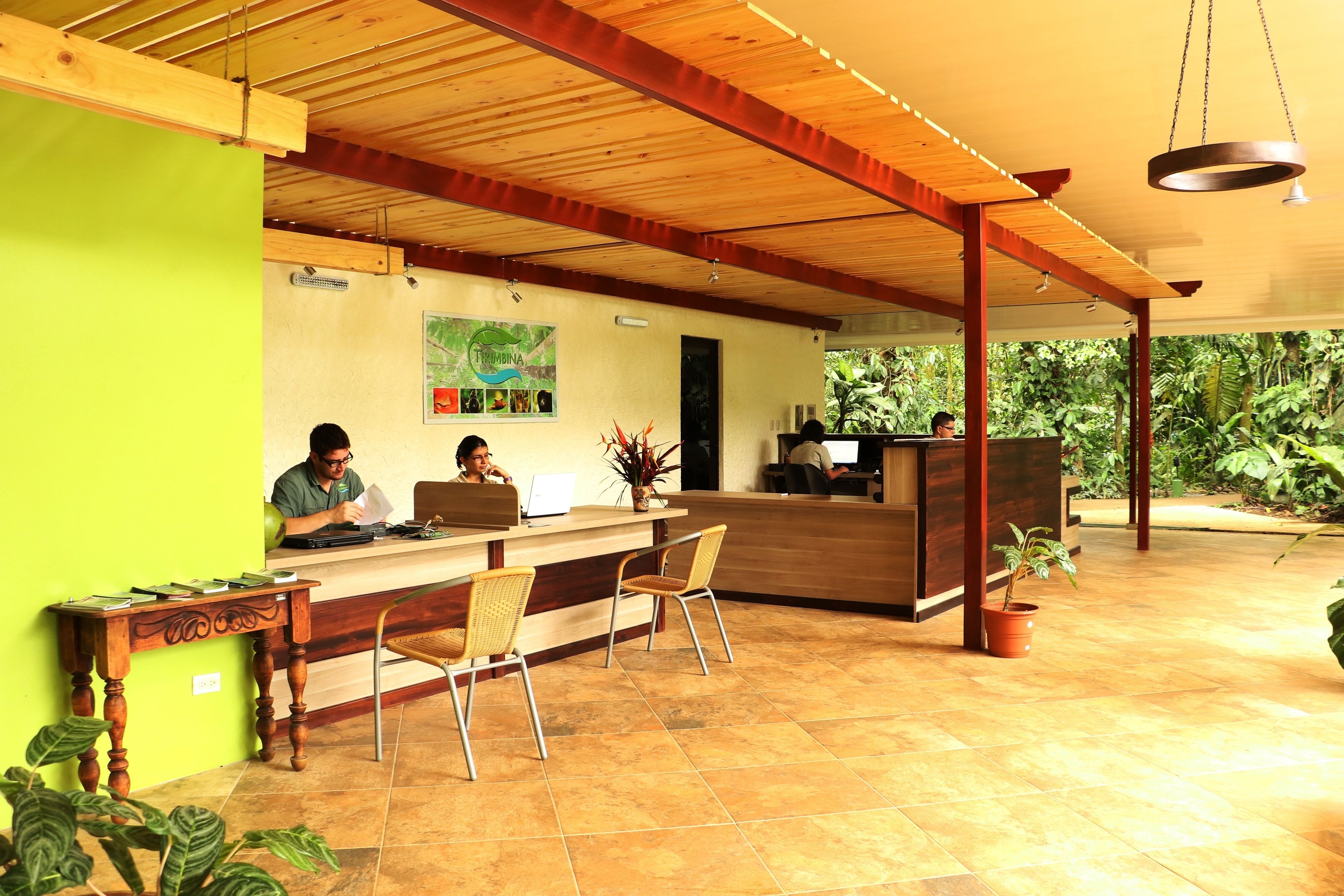 A reception area with a wooden ceiling, a reception desk, two chairs, and a potted plant.