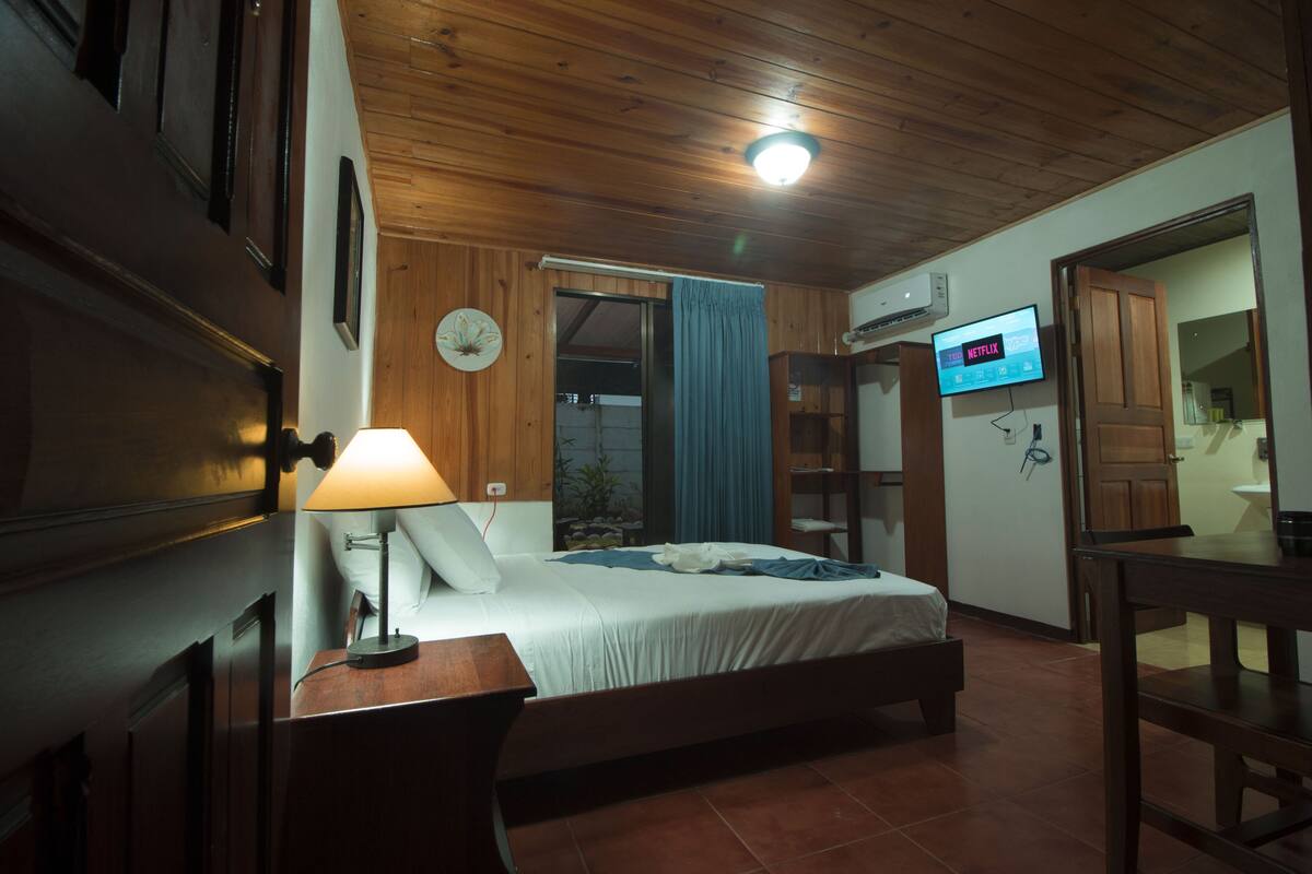 Un dormitorio con una cama, un escritorio, una lámpara, un televisor y una puerta que da a un baño.