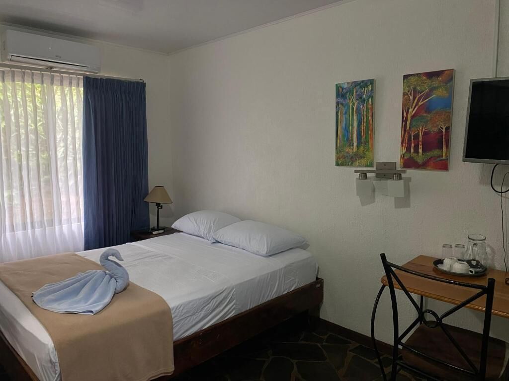 Een hotelkamer met een bed, een bureau, een stoel, een televisie en twee schilderijen aan de muur.
