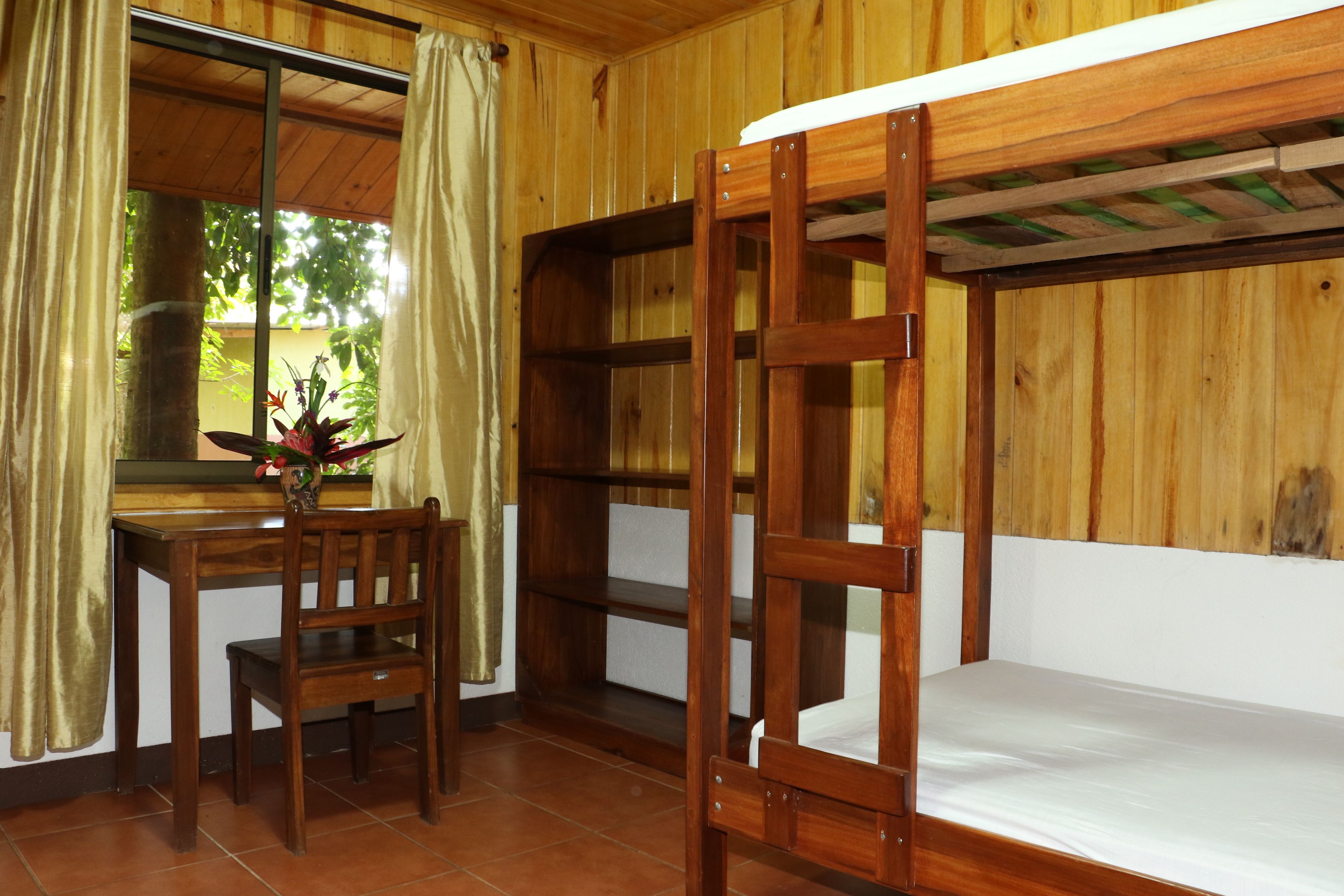 A wooden room with bunk beds, a desk, and a chair.
