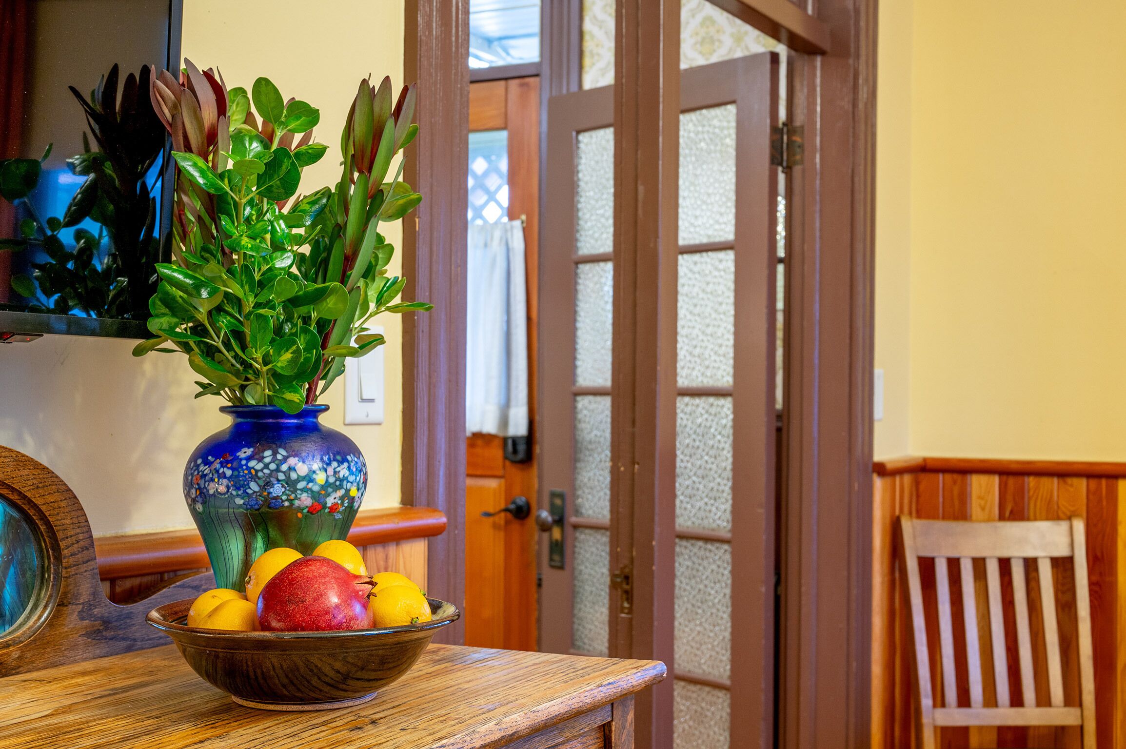Una mesa de madera con un cuenco de fruta y un florero de plantas verdes.