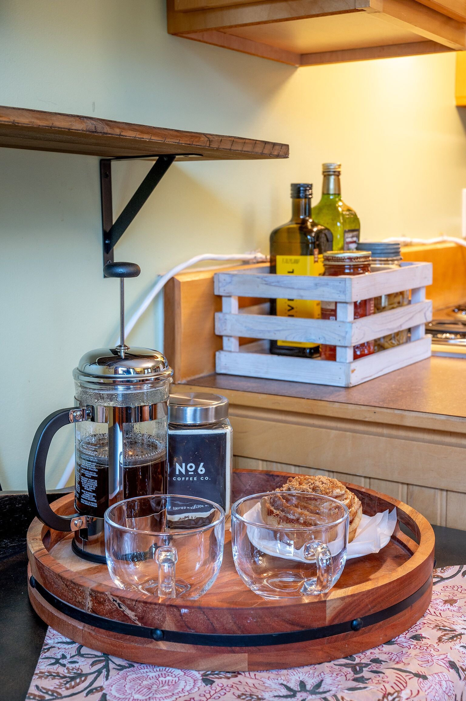 A wooden tray with a coffee maker, a glass, and a pastry on a table.