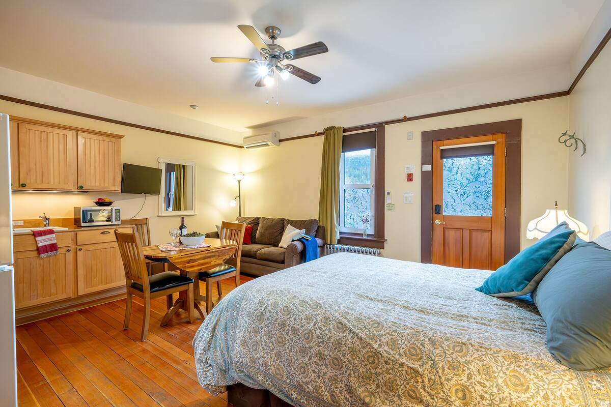 Ein Schlafzimmer mit Bett, Schreibtisch, Stuhl, Sofa und einer Küchenzeile mit Holzsärchen und Mikrowelle.