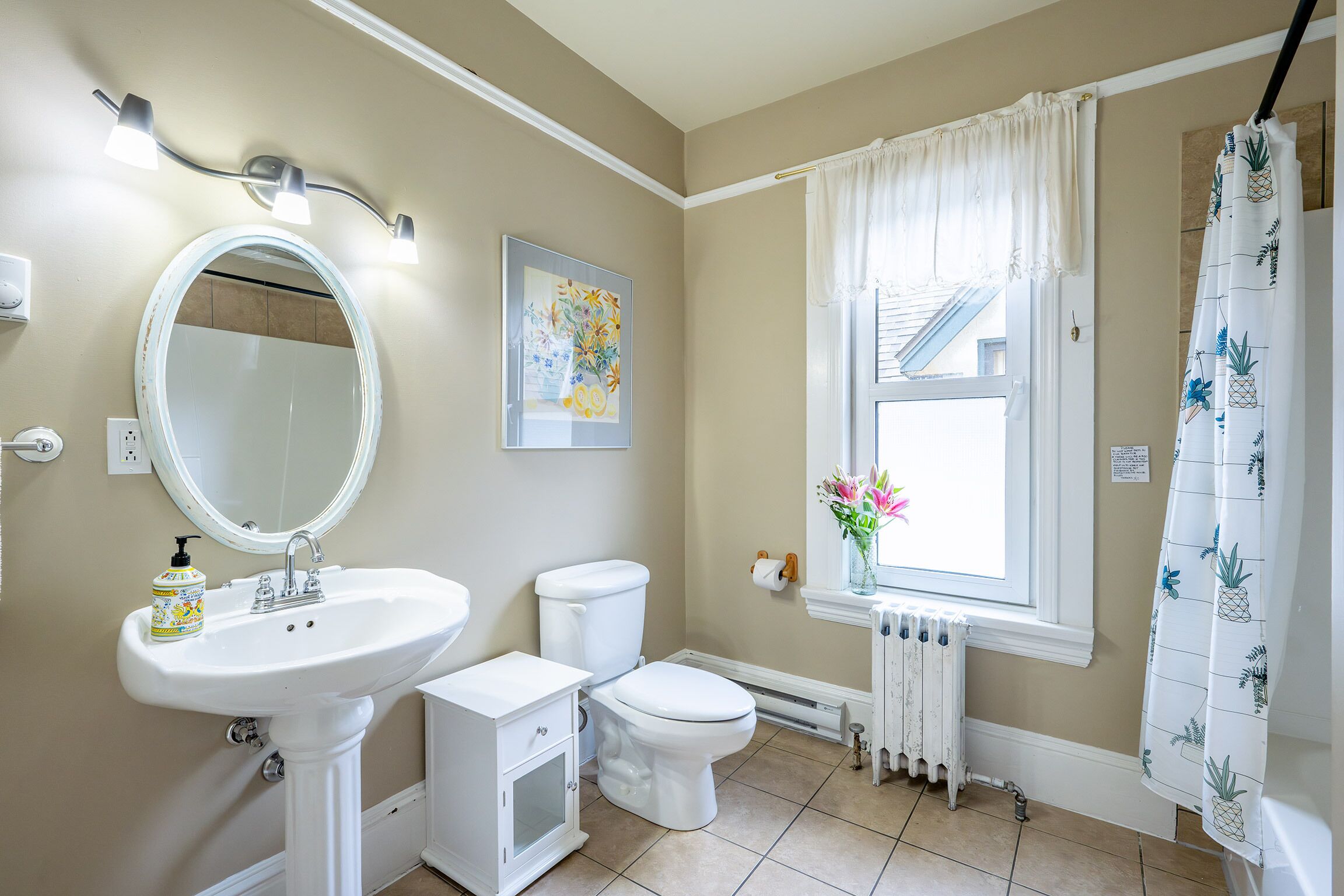 A bathroom with a pedestal sink, toilet, and a window with a view of the outside.