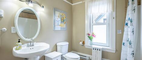 A bathroom with a pedestal sink, toilet, and a window with a view of the outside.