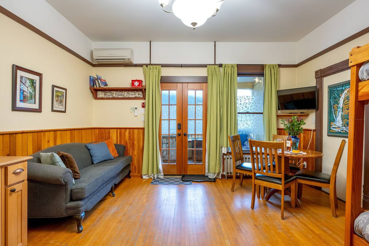 Ein gemütliches Wohnzimmer mit einer Couch, einem Esstisch mit Stühlen, einem Fernseher und einem Holzschrank.