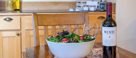 A wooden dining table with a white bowl of salad and a bottle of Wente wine.