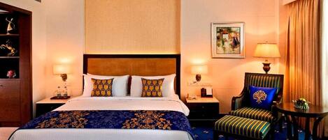 Ein Hotelzimmer mit einem großen Bett, zwei Nachttischen, einem Sessel, einem Schreibtisch und einem Gemälde an der Wand.