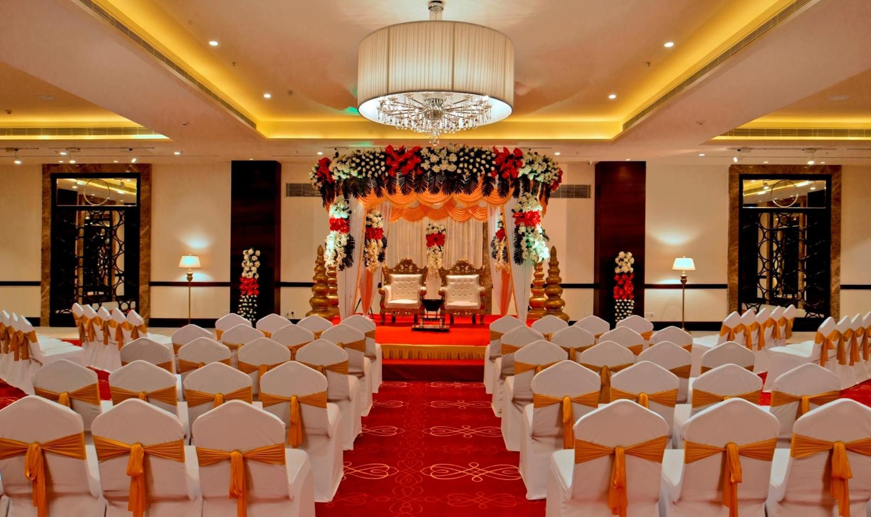 A banquet hall with rows of white chairs, a red carpet, and a stage with floral decorations.