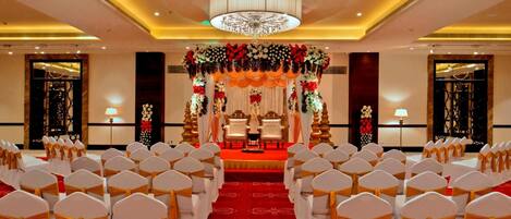 A banquet hall with rows of white chairs, a red carpet, and a stage with floral decorations.