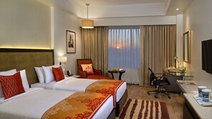 Een hotelkamer met twee bedden, een bureau, een stoel, een klein tafeltje met fruit en uitzicht op de ondergaande zon door het raam.