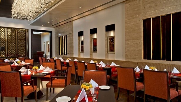 Een restaurant met meerdere tafels, gedekt met rode tafelkleden en oranje stoelen.
