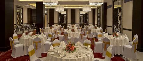 Une salle de banquet avec des tables rondes, des nappes blanches, des rubans dorés et des lustres.
