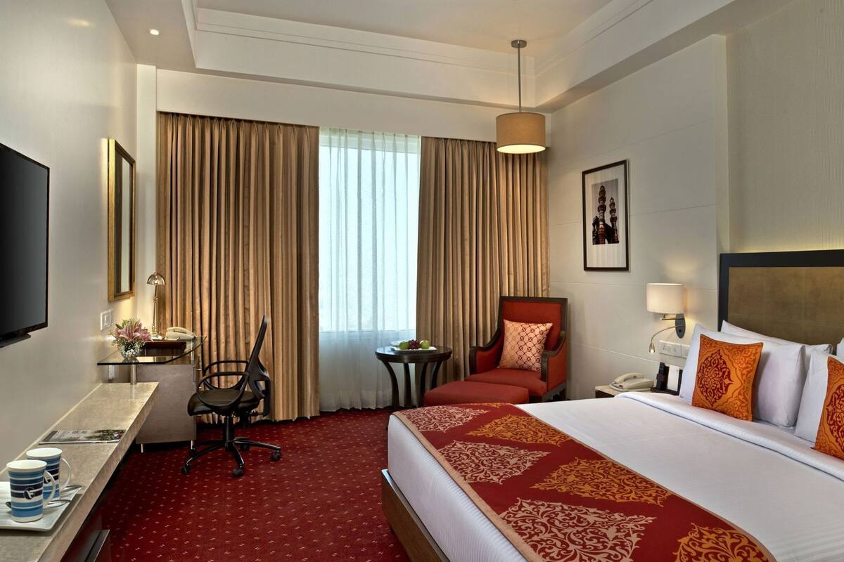 Ein Hotelzimmer mit Bett, Schreibtisch, Stuhl, Fernseher und einem Fenster mit Vorhängen.