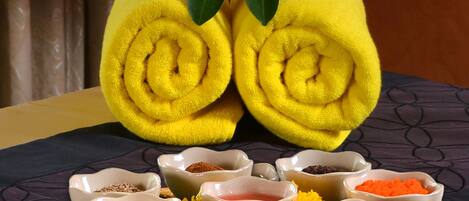 A set of yellow towels with a flower on top, placed on a woven mat with bowls of various powders and herbs.