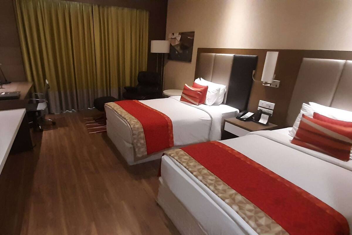 Hotelkamer met twee bedden, een bureau, een stoel, een lamp, een televisie en een raam met gordijnen.
