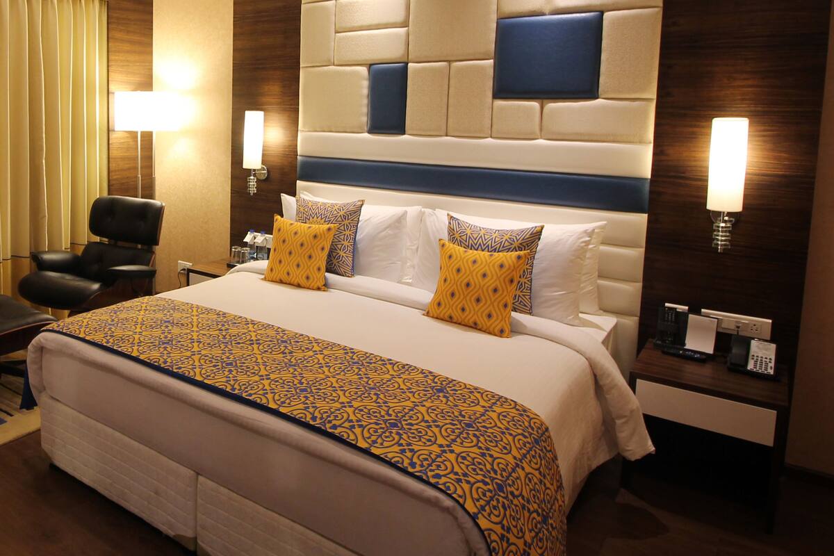 Een hotelkamer met een groot bed, een bureau met lamp, een stoel en een raam met gordijnen.