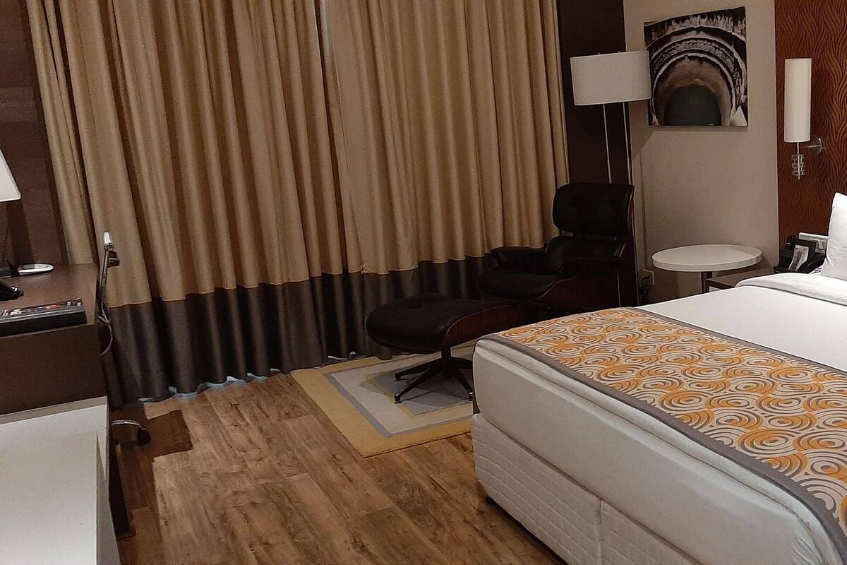 Een hotelkamer met een groot bed, een bureau, een stoel, een bijzettafeltje en een gordijn.