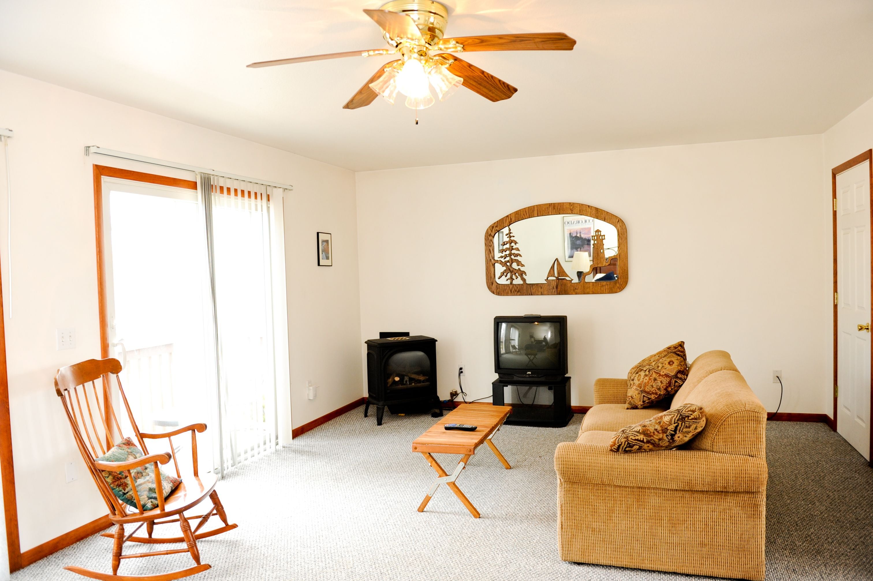 A living room with a rocking chair, a sofa, a television, a fireplace, and a ceiling fan.