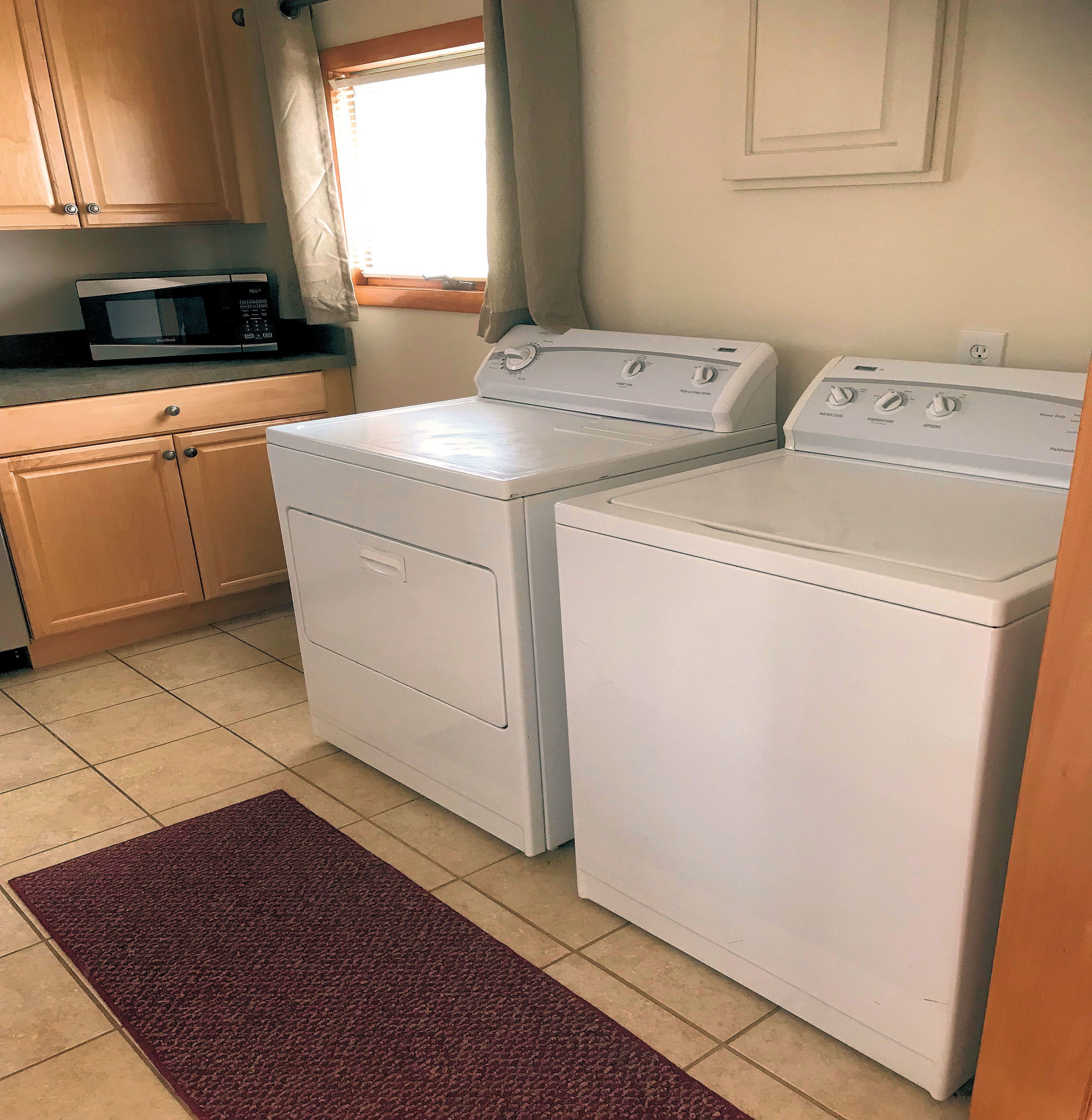 A laundry area with two white washing machines, a microwave, and wooden cabinets.