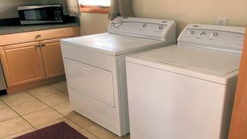 A laundry area with two white washing machines, a microwave, and wooden cabinets.