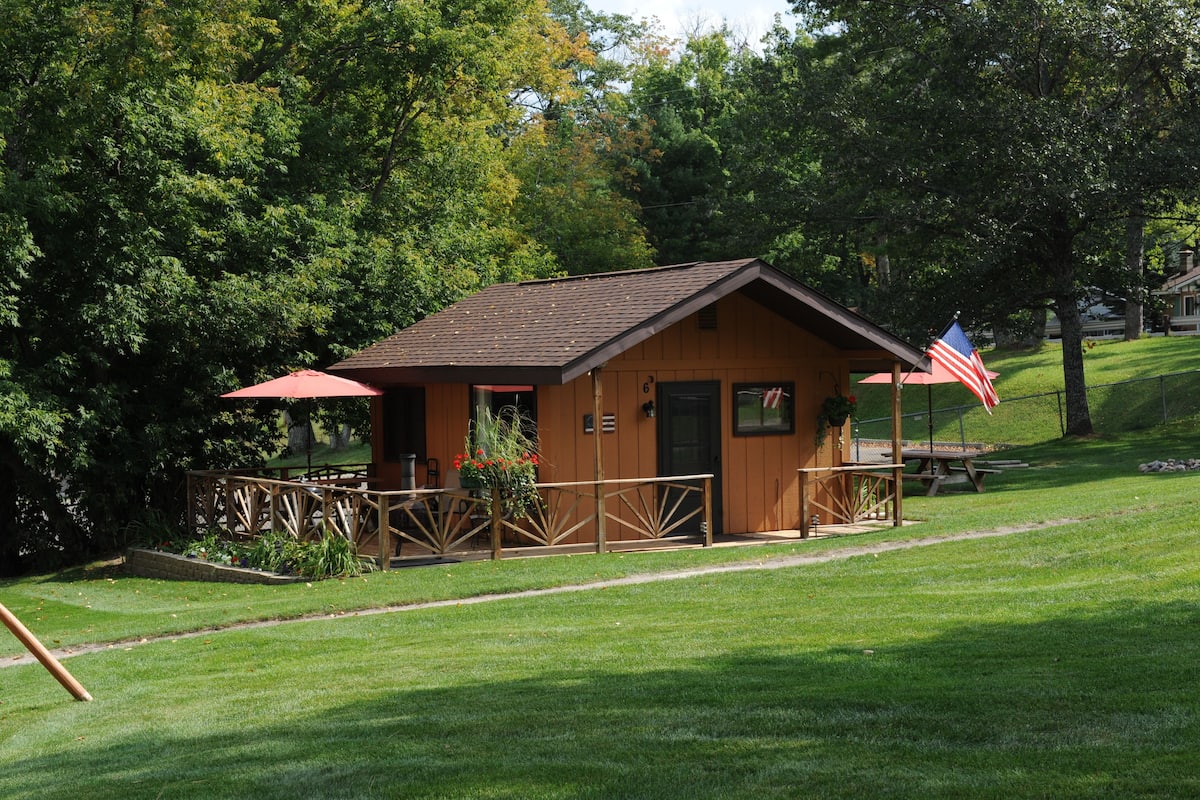 A small wooden cabin with a porch, a picnic table, and an American flag.